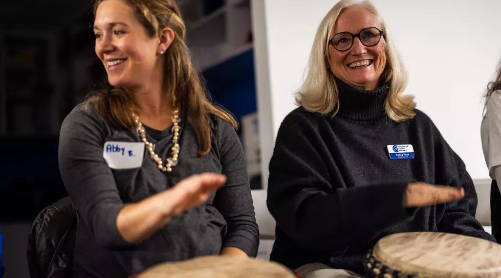 Two women playing hand drums for community building at the AllyCamp volunteer training event.