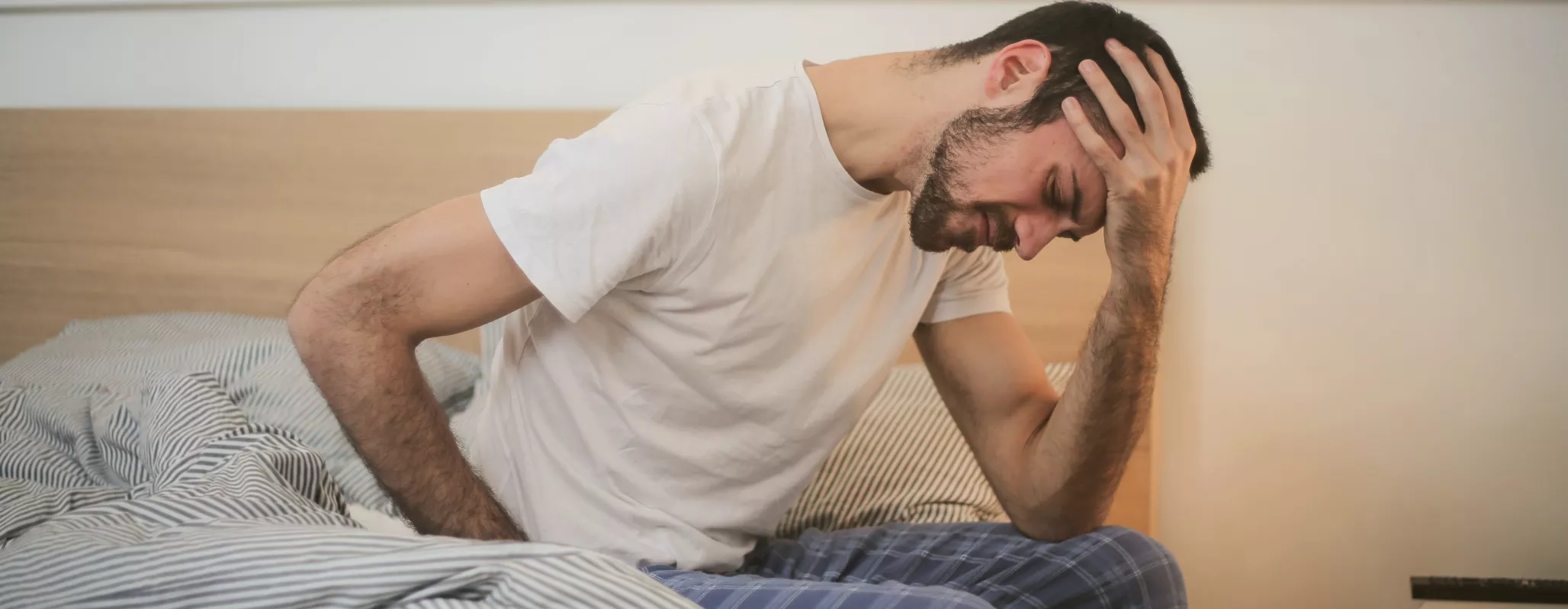 man grimacing on side of bed