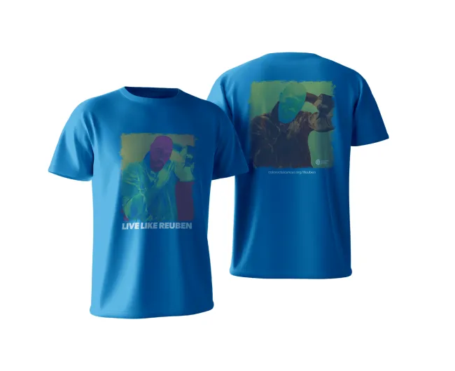 Front and back view of a bright blue T-shirt featuring a stylized, color-treated portrait of a man posing with one hand behind his head. The front includes the text “LIVE LIKE REUBEN” in bold white letters beneath the image. The back shows a larger version of the portrait with the Colorectal Cancer Alliance logo and the URL “colorectalcancer.org/Reuben” printed below.